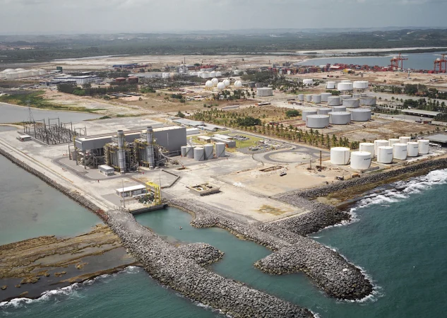 Vista aérea de usina de geração de energia à beira-mar, com tanques de armazenamento e porto ao fundo