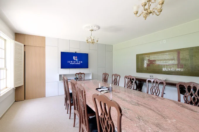 Sala de reunião da Juridicon, com mesa de mármore, cadeiras de madeira e a marca na tela