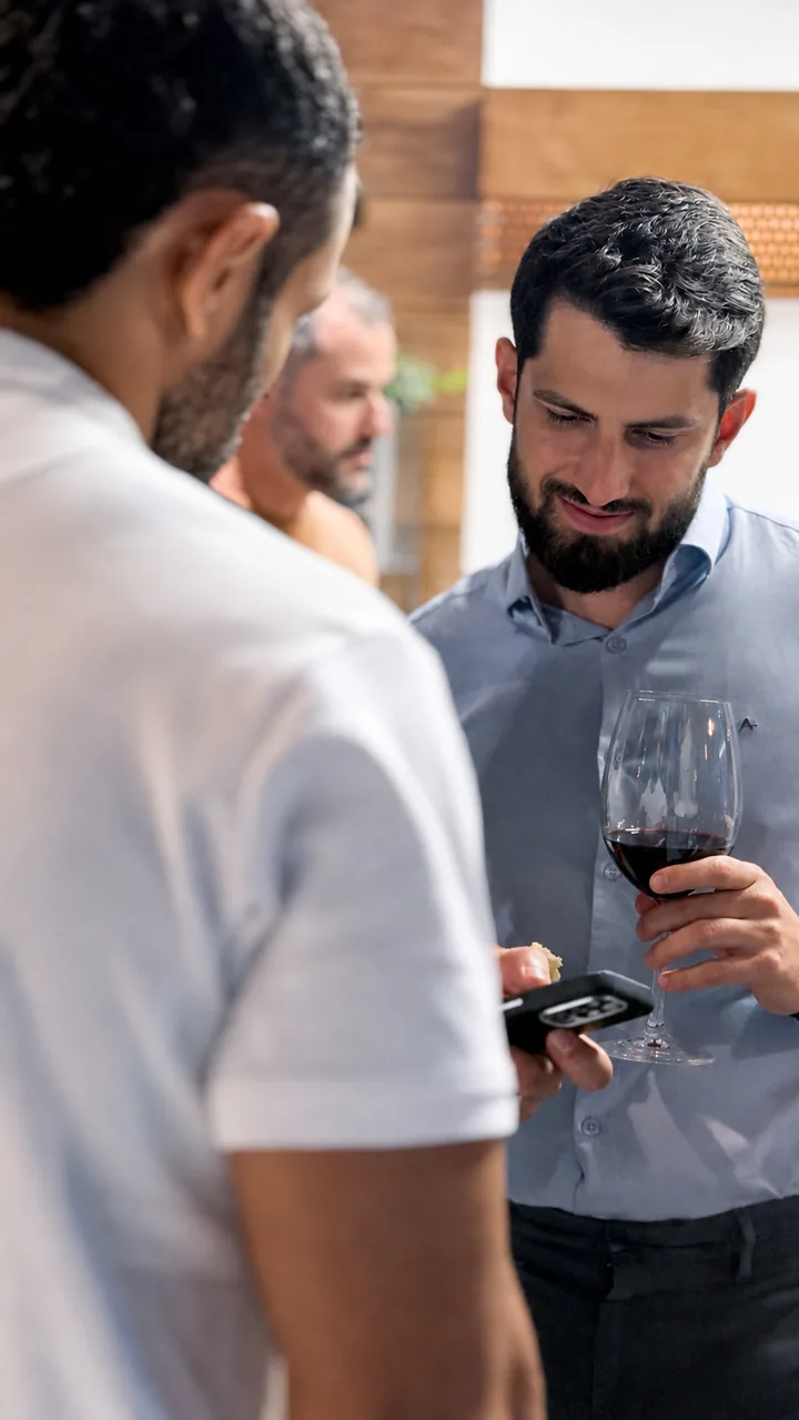 Convidado com taça de vinho e celular conversando durante encontro da Fato Analytics