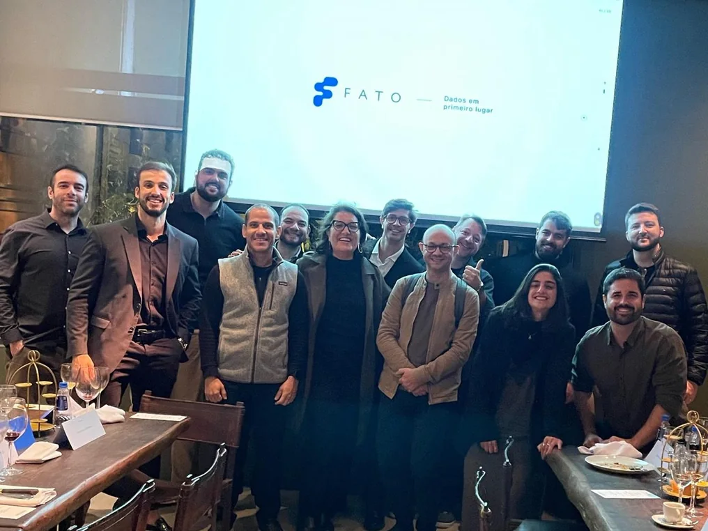Grupo de participantes de um treinamento da Fato reunido em frente ao slide com a marca Fato e a tagline Dados em primeiro lugar