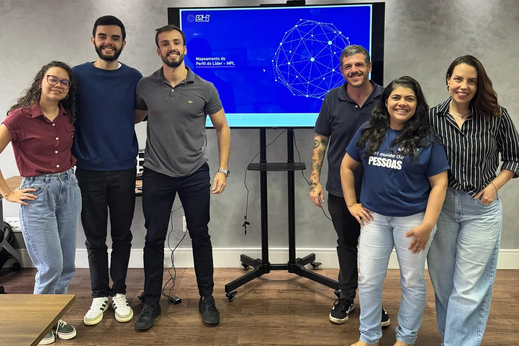Turma de um treinamento in company da Fato posando em frente à tela com a apresentação, na sala de reunião da empresa
